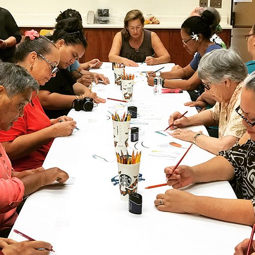 Kūpuna coloring mosaic mural panels together around a table